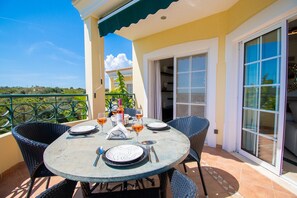 A round table with chairs, a bottle of wine, and glasses on a balcony with a view.
