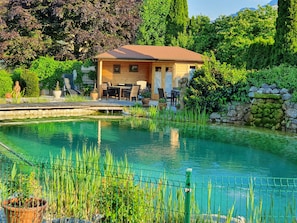 Un área de piscina al aire libre tranquila con una terraza de madera, asientos y un muro de piedra.
