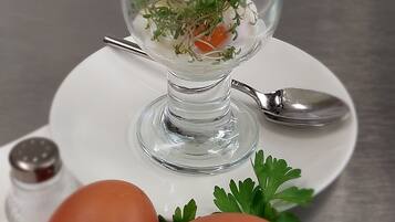 Un recipiente de vidrio transparente con un huevo blanco y hierbas verdes sobre un plato blanco, acompañado de dos huevos enteros y una ramita de perejil.
