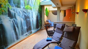 Un área de spa con un mural de cascada, sillones reclinables y un rincón de estar con una mesa y sillas.