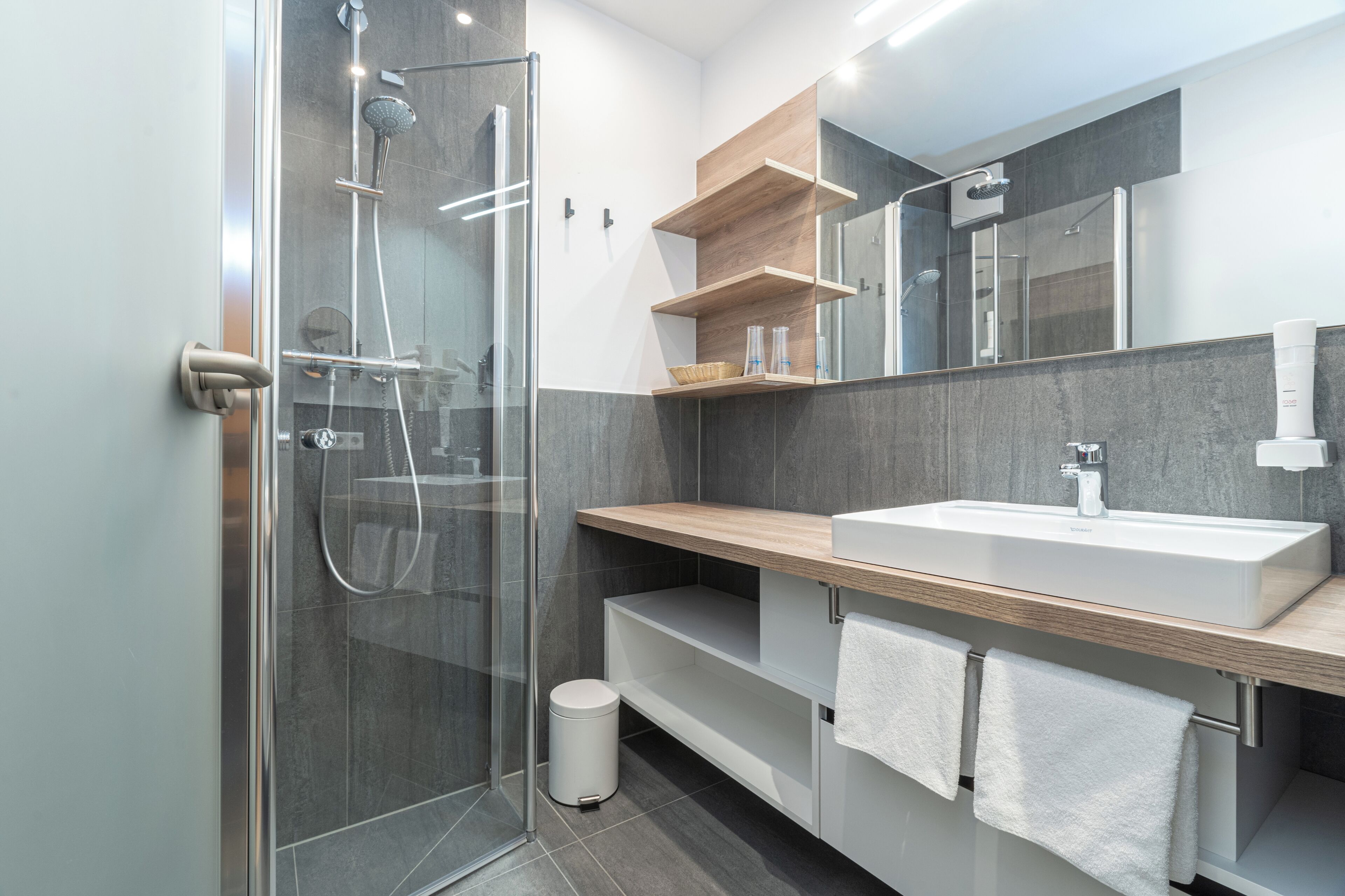 Une salle de bain moderne avec une douche à parois de verre, un lavabo blanc et des étagères en bois.