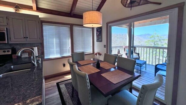 Una zona pranzo con tavolo e sedie, una cucina con pensili ed elettrodomestici, e vista su una terrazza esterna attraverso una porta scorrevole in vetro.