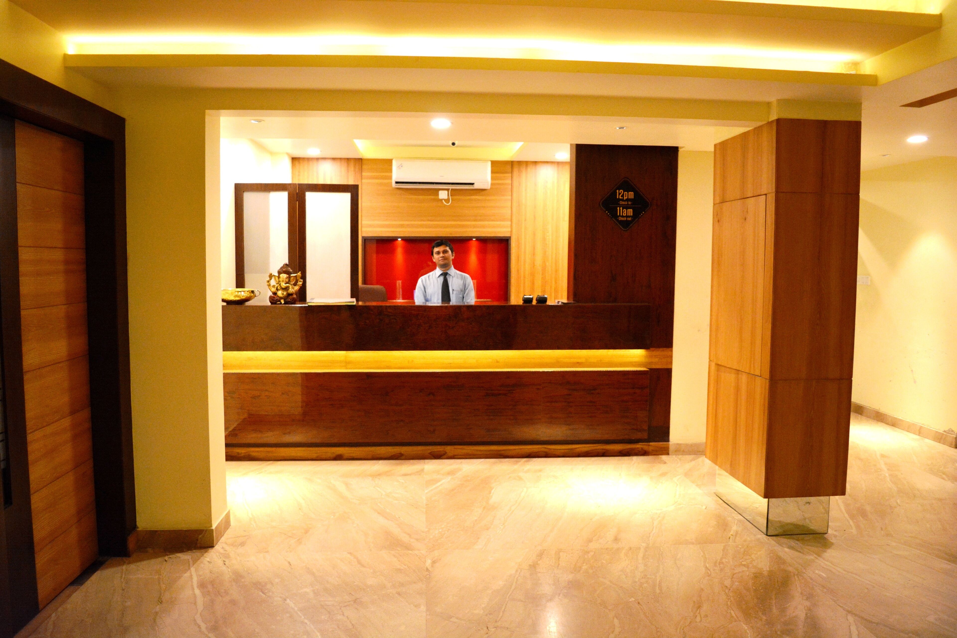 A reception area with a wooden reception desk, a man standing behind it, and a clock indicating 12:11 pm.
