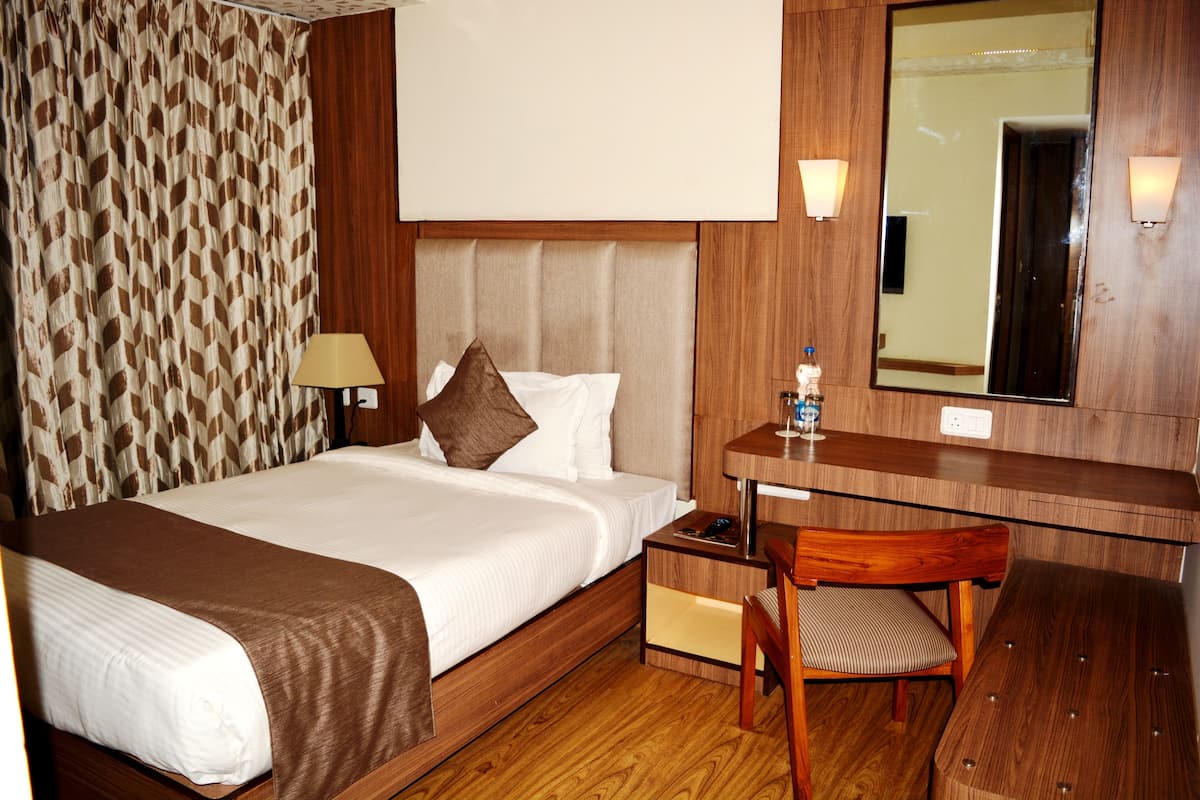 A hotel room with a bed, bedside table, chair, and a mirror.