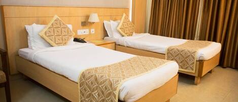 Two single beds with wooden frames and white bedding, a bedside table with a lamp, and a power outlet on the wall.