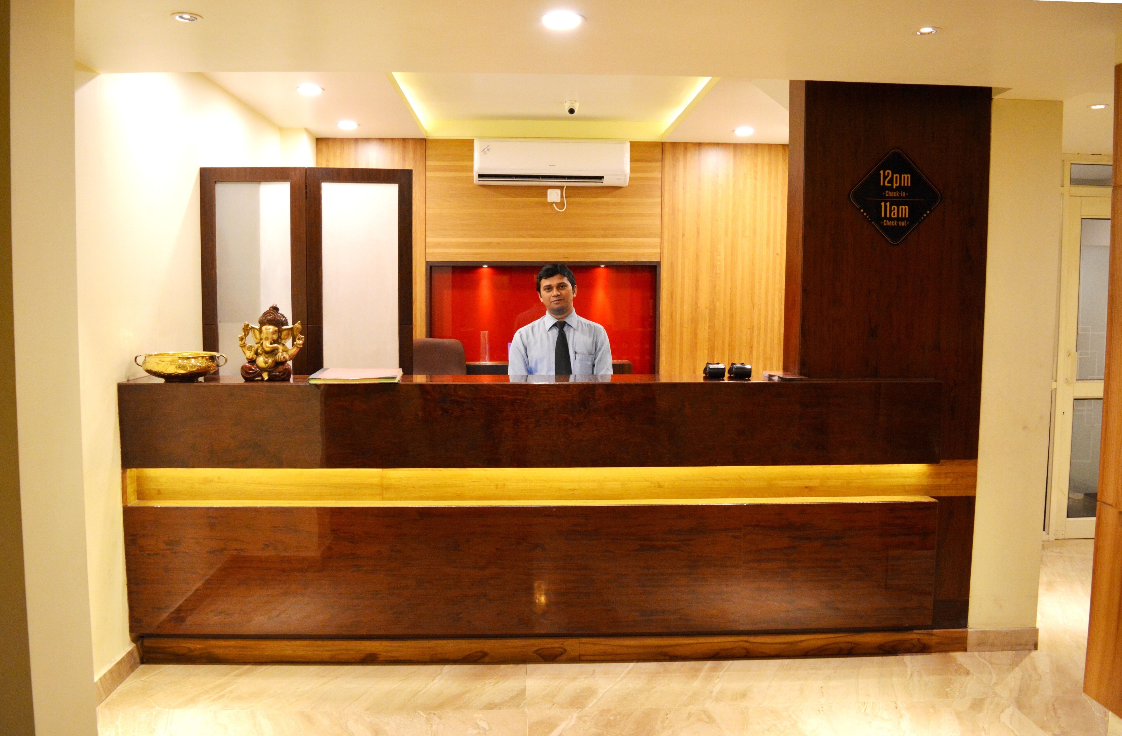 A reception desk with a man standing behind it, wooden paneling, a sign indicating check-in times, and a large mirror above the desk.