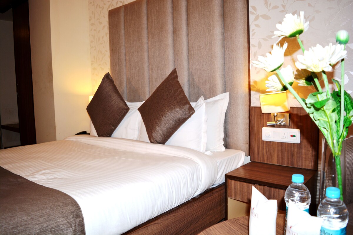 Una habitación de hotel con una cama, mesita de noche y un jarrón con flores.