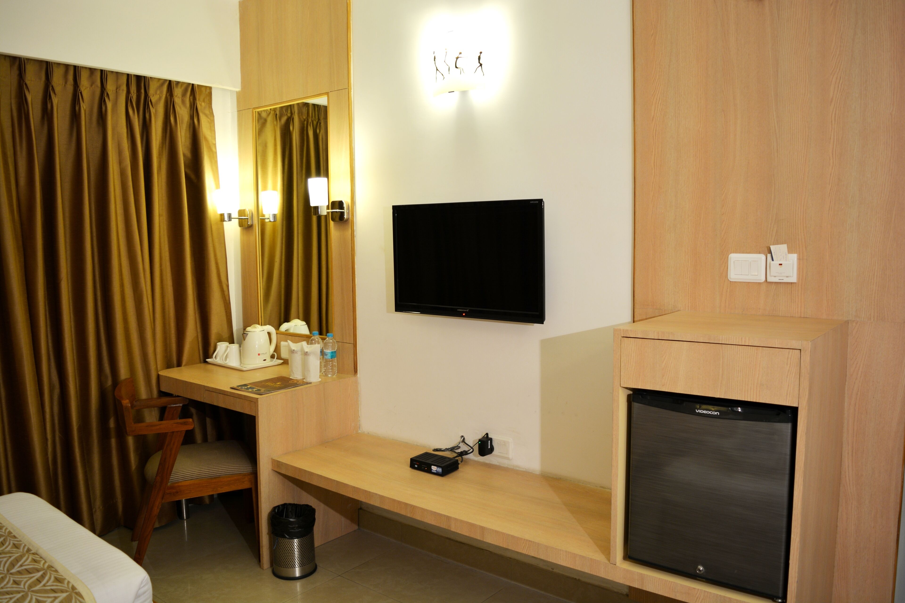 A hotel room with a bed, a desk with a chair, a television, and a minibar.