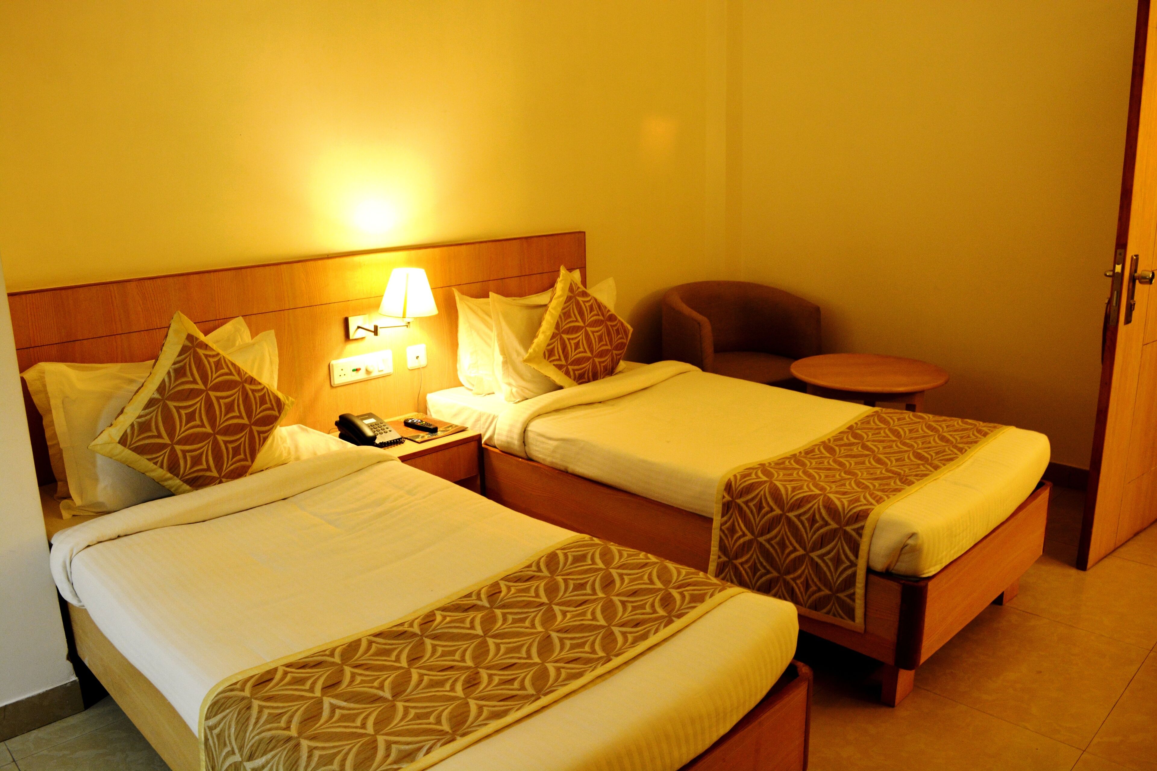Une chambre d’hôtel avec deux lits, une table de chevet avec une lampe, une chaise et une petite table.