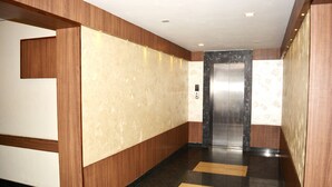 A modern elevator with a metallic finish, a wooden panel wall, and a marble-like floor.
