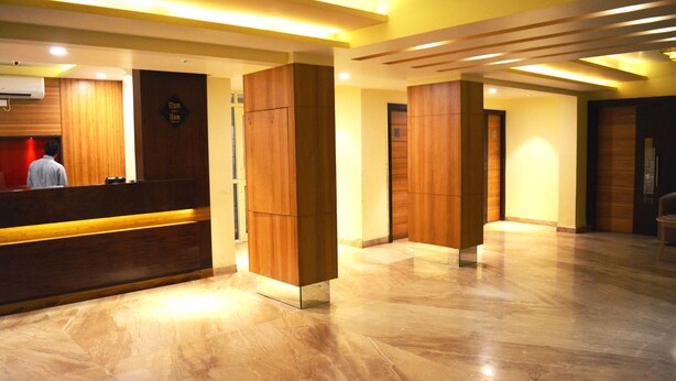 A hotel reception area with a wooden reception desk, a digital clock displaying 12pm and 11am, and a polished marble floor.