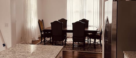 Une cuisine dotée d’un plan de travail en granit, de meubles en bois, d’un réfrigérateur en acier inoxydable et d’un coin repas avec une table et des chaises.