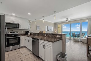 Cozinha moderna com eletrodomésticos de aço inoxidável, bancada de granito e vista para a varanda.