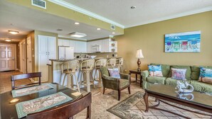 A spacious living room with a dining area, a kitchen, and a green sofa with colorful cushions. - Upgrade to a Getaway! (Panama City Beach)