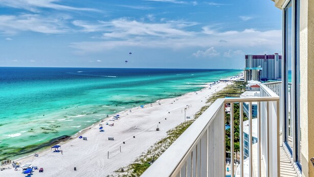 A beach view from a balcony with a clear sky, turquoise water, and a sandy beach with umbrellas. - Upgrade to a Getaway! (Panama City Beach)