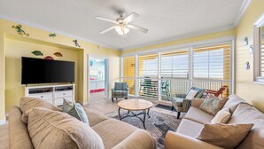 Un salon comprenant un canapé, un téléviseur, un ventilateur de plafond et un balcon aménagé avec du mobilier d’extérieur.