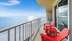 Un balcon avec des fauteuils Adirondack rouges donnant sur une plage.