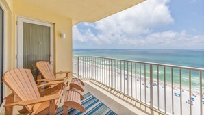Un balcon avec des chaises en bois, une vue sur la plage et un ciel dégagé.