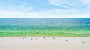 A beach with clear turquoise water, a sandy shore, and a few umbrellas. - Upscale but Within Reach on the Beach! (Panama City Beach)