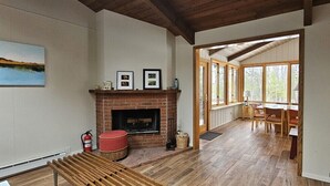 Ein Zimmer mit Kamin, Holzboden, einer Essecke mit Stühlen und großen Fenstern.