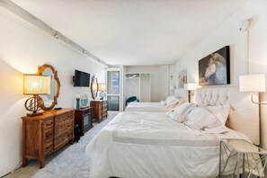 A hotel room with two beds, a television, a dresser, and a painting on the wall.