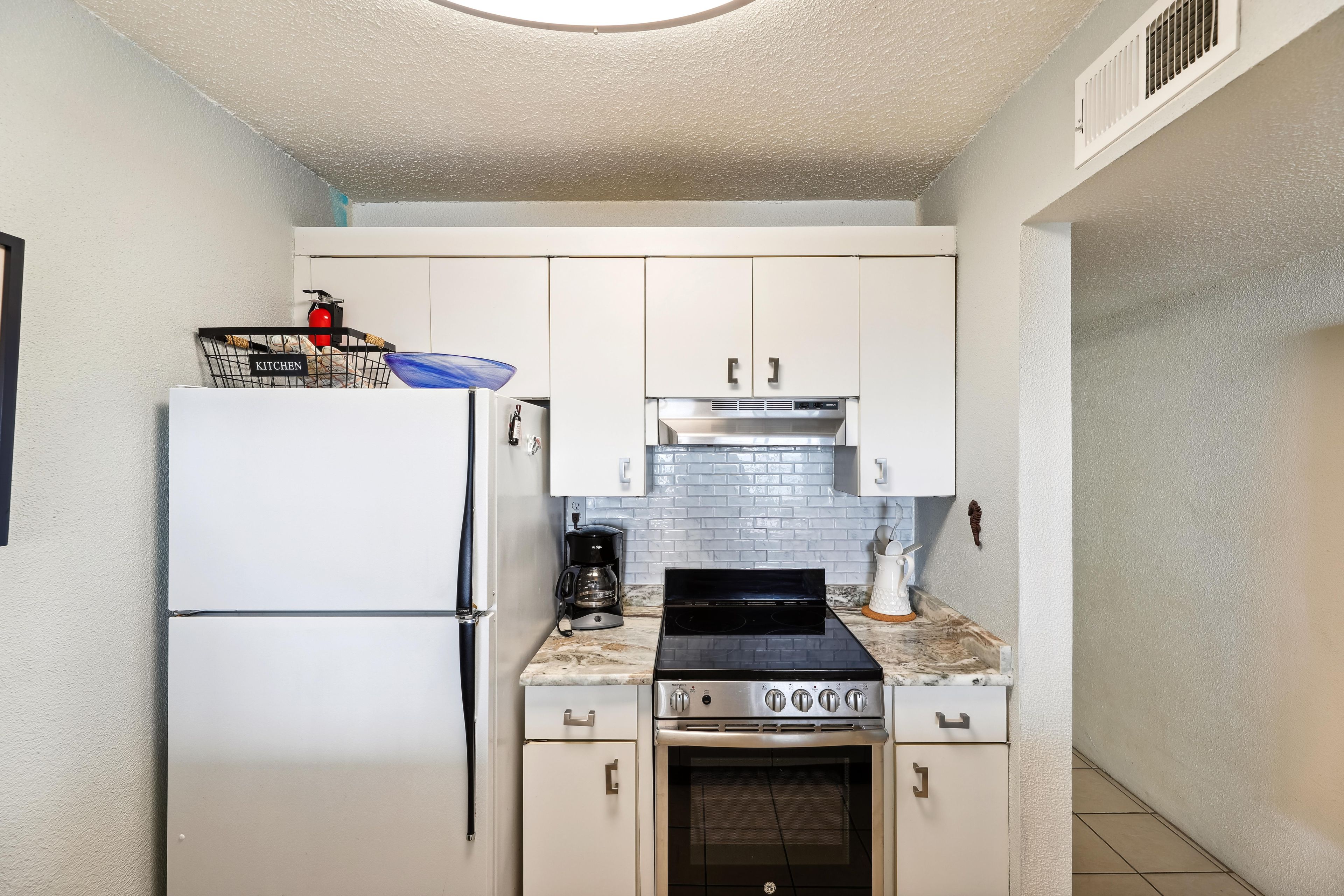 A compact kitchen with white cabinets, a stainless steel stove, a coffee maker, and a refrigerator.