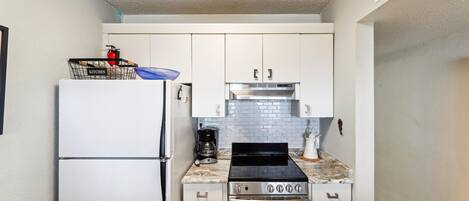 A compact kitchen with white cabinets, a stainless steel stove, a coffee maker, and a refrigerator.