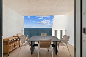 Un balcon avec une table et des chaises, un fauteuil en osier et une vue sur la mer.