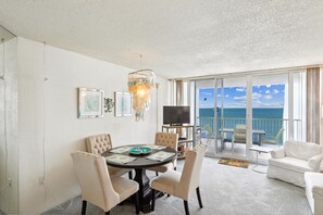Una habitación con una mesa redonda, sillas, un televisor y un balcón con vistas al mar.