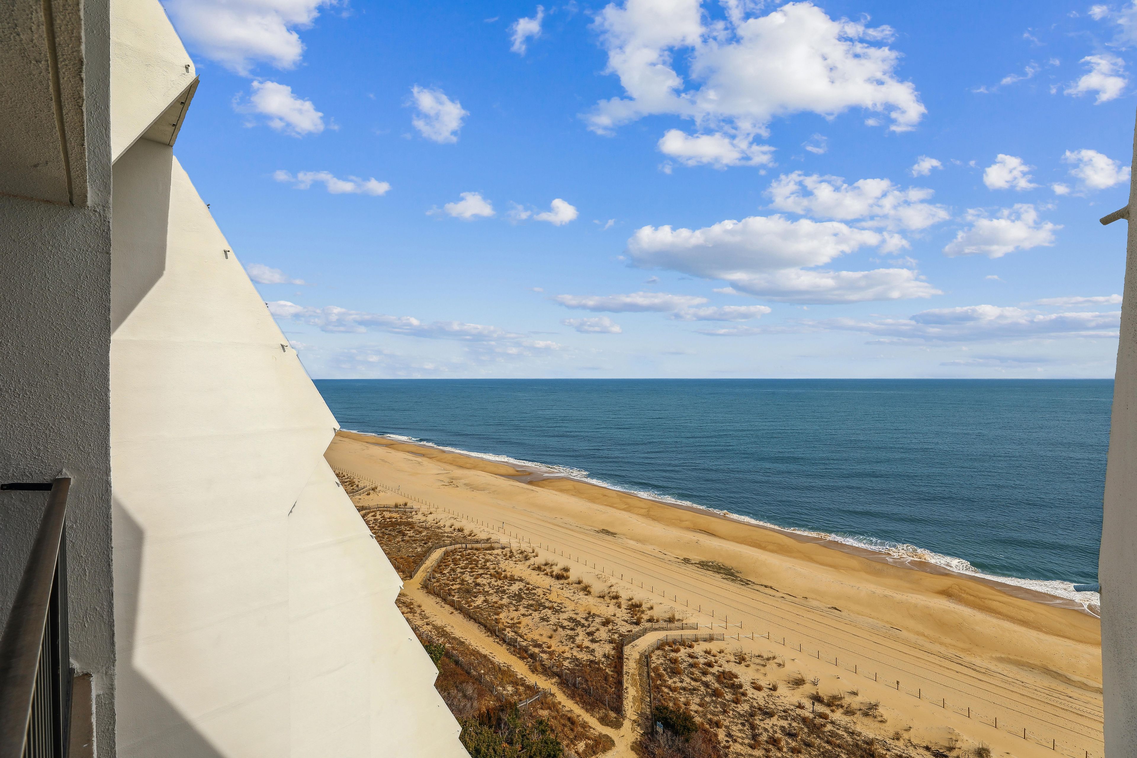 Une vue sur la plage depuis un balcon, avec un ciel dégagé et l’océan à l’horizon.