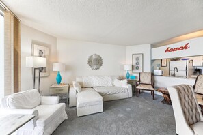 A modern hotel room with a sofa, a chair, a desk, and a kitchenette area.
