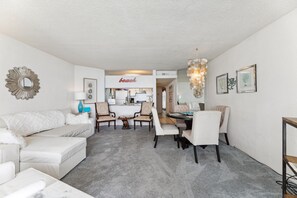 Un salon moderne avec un canapé blanc, une table à manger avec des chaises, et une cuisine en arrière-plan.