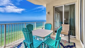 A balcony with a table and chairs, a view of the ocean, and a sliding glass door leading to a room. - Huge Balcony, Huge Fun Awaits in Popular Beachfront Condo! (Panama City Beach)
