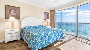 A bedroom with a large bed, two bedside tables with lamps, a ceiling fan, and a balcony with a view of the ocean. - Unwind to Visions of the Sea (Panama City Beach)
