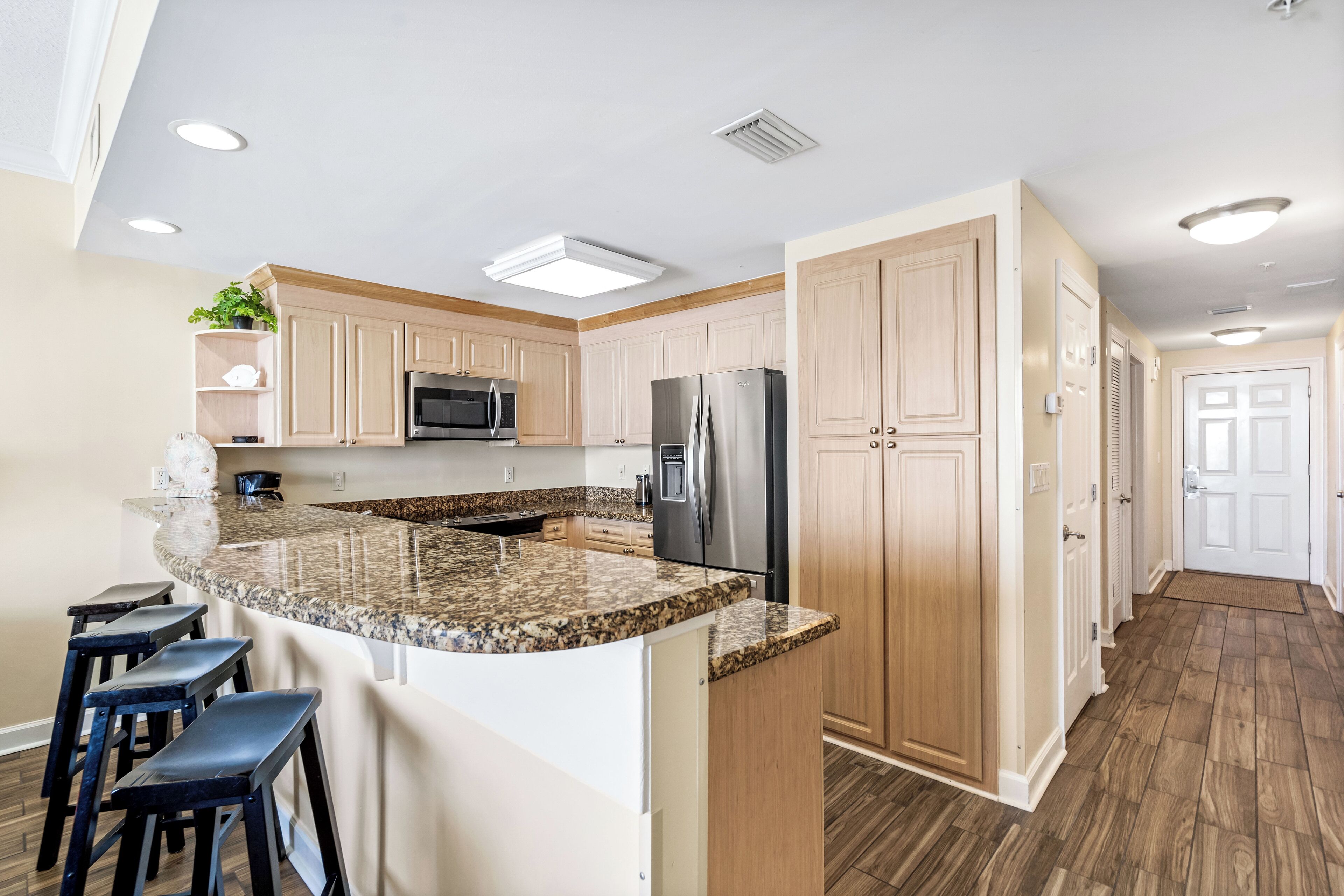 A kitchen with granite countertops, stainless steel appliances, wooden cabinets, and a bar area with stools.