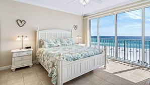 A bedroom with a bed, nightstands, a ceiling fan, and a view of the beach. - Sleep Six and Splash by the Sea! (Panama City Beach)