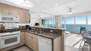 Una cocina moderna con encimeras de granito, electrodomésticos de acero inoxidable y vistas al océano a través de amplias ventanas.