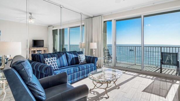 Una sala de estar moderna con un sofá grande, una mesa de centro y un televisor. La habitación tiene ventanas amplias con vistas al mar.