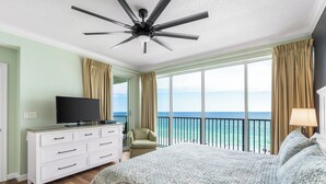 A hotel room with a large bed, a TV on a white dresser, a ceiling fan, and a balcony with a view of the ocean. - Deluxe Beachfront Condo (Panama City Beach)