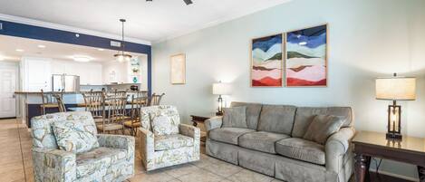 Un salon comprenant un canapé, deux fauteuils, un coin repas avec des chaises, un ventilateur de plafond et des œuvres d’art accrochées au mur.