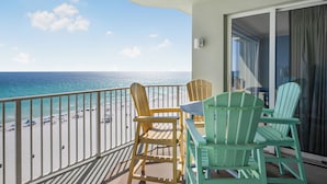 A balcony with a view of the beach, featuring wooden chairs and a table. - Deluxe Beachfront Condo (Panama City Beach)