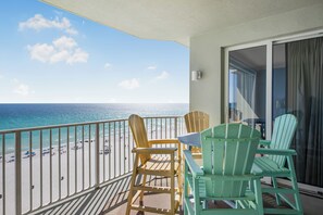 A balcony with a view of the beach, featuring wooden chairs and a table.