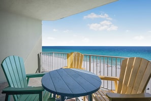 A balcony with a view of the ocean, featuring a round table and four Adirondack chairs.