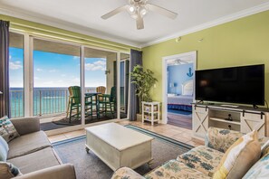 A room with a balcony, a television, a sofa, and a dining area.