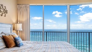 A bedroom with a large bed, a nightstand with a lamp, and a view of the ocean through a balcony. - Updated Condo on Miles of Beach! (Panama City Beach)