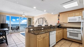 A kitchen with wooden cabinets, a microwave, a dishwasher, and a large window overlooking a balcony. - Updated Condo on Miles of Beach! (Panama City Beach)