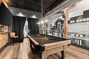 A pool table in a room with a cityscape mural, a brick wall, and a wooden ceiling.