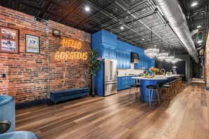 A modern kitchen with blue cabinets, a neon sign, and a bar area with stools.