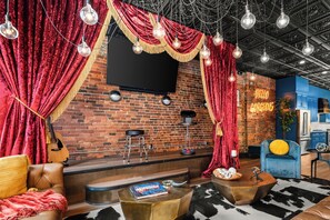 Ein gemütlicher Lounge-Bereich mit Backsteinwand, roten Vorhängen, einem Flachbildfernseher und einem Neonzeichen.