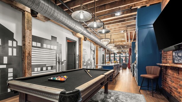 Une table de billard avec des billes, un coin bar avec des tabourets et un mur en briques.